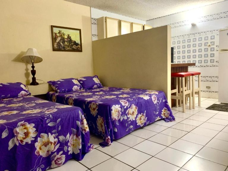 Habitación doble con camas de edredón morado floral en Garden Beach Resort con zona de cocina