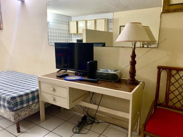 Habitación con escritorio blanco, televisor, lámpara y radio Sony en Garden Beach Resort