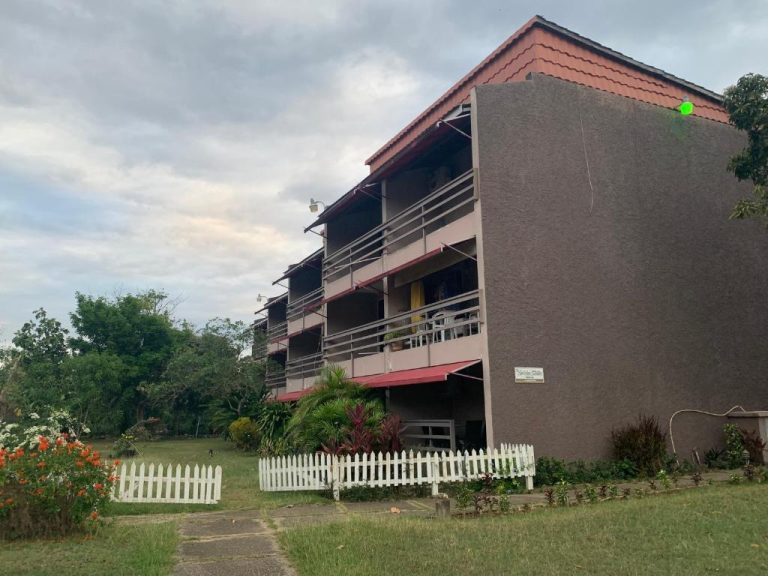 Fachada exterior del Garden Beach Resort con jardines tropicales, balcones y valla blanca