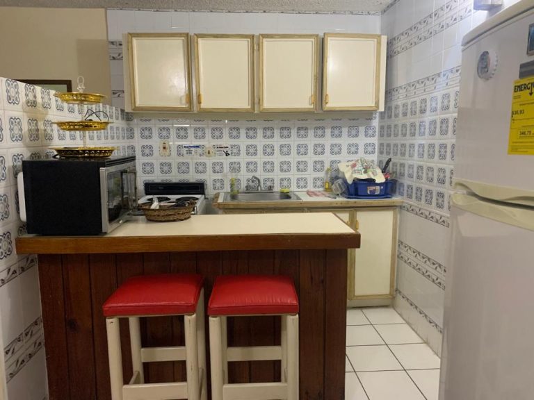 Cocina equipada con barra desayunador y taburetes rojos en Garden Beach Resort