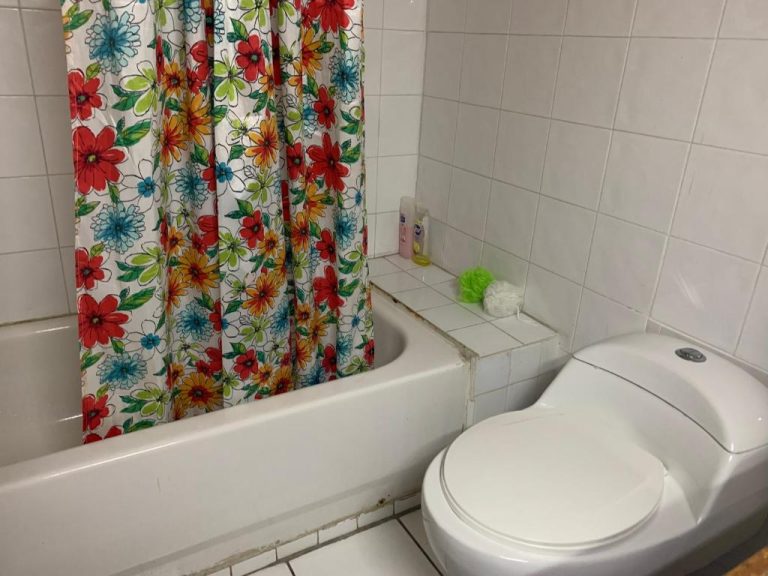 Baño con bañera y cortina floral del Garden Beach Resort, con inodoro y accesorios de ducha