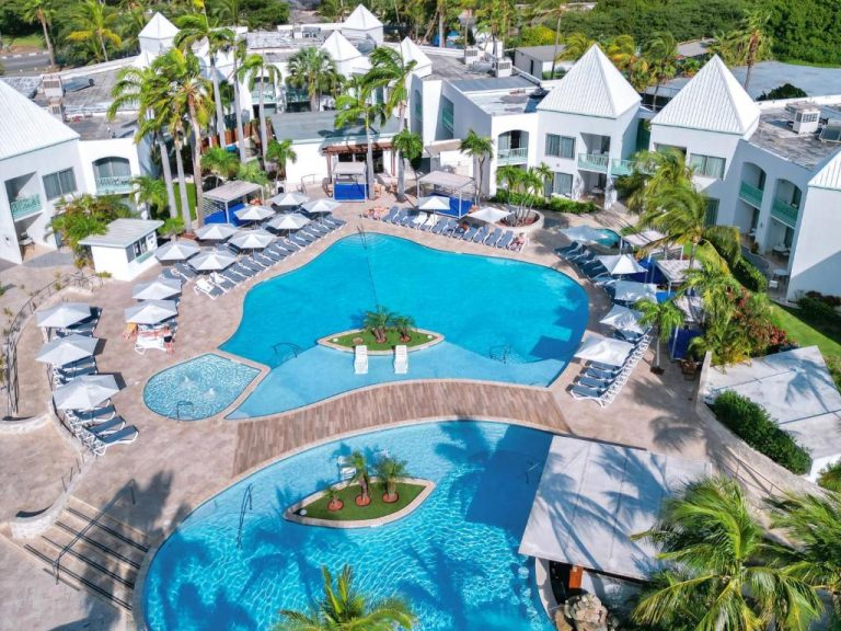 Vista aérea de las piscinas exteriores con palmeras y tumbonas del The Mill Resort and Suites