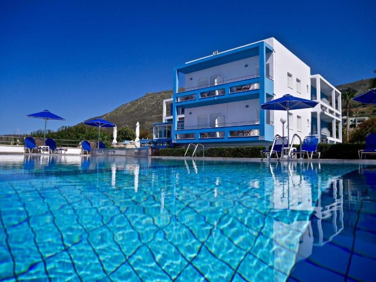 Piscina exterior cristalina con tumbonas azules y edificio blanco en Kanakis Blue Beach Apartments, Grecia