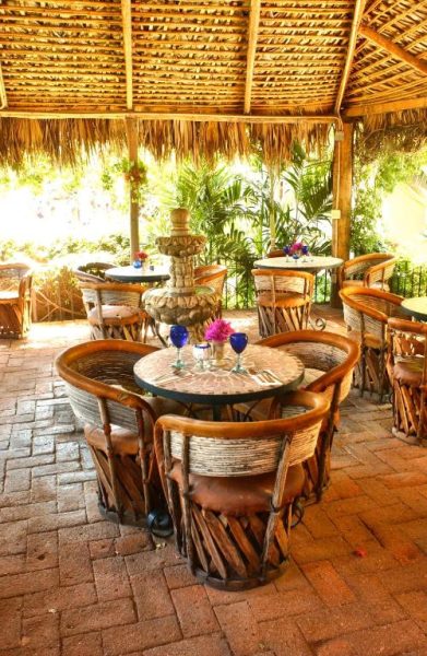 Terraza restaurante con techo de palapa y mesas rústicas de madera en The Bungalows Hotel