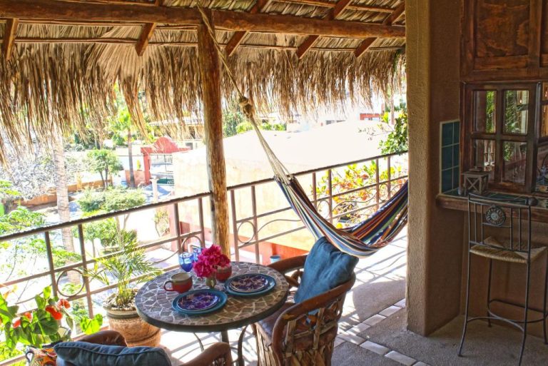 Terraza con hamaca colorida y palapa de palma en The Bungalows Hotel con vista al jardín tropical