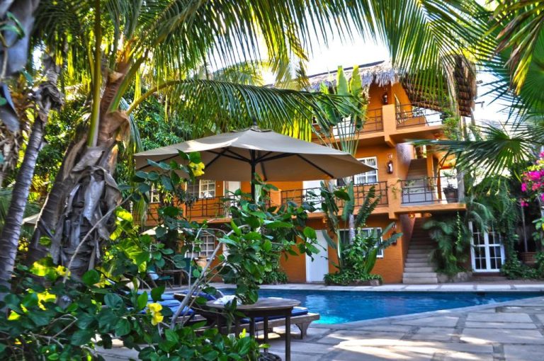 Piscina exterior rodeada de vegetación tropical y sombrillas en The Bungalows Hotel