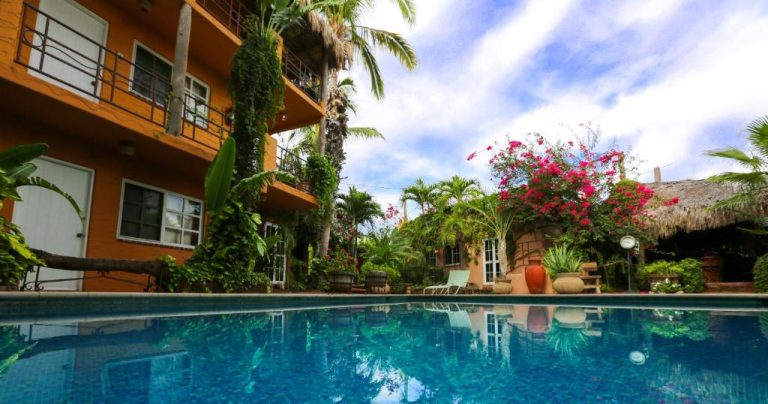 Piscina exterior rodeada de jardín tropical y palmeras en The Bungalows Hotel con bougainvillea rosa