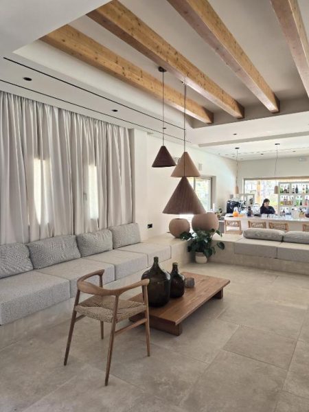 Amplio salón con vigas de madera y sofás grises en Aegean Houses con zona de bar al fondo
