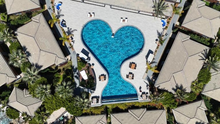 Vista aérea de la piscina con forma de corazón del Porto Amore Club Hotel rodeada de villas y palmeras