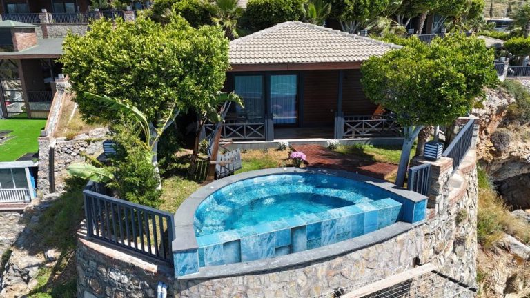 Piscina privada redonda con vistas al mar en Porto Amore Club Hotel rodeada de jardín y bungalow