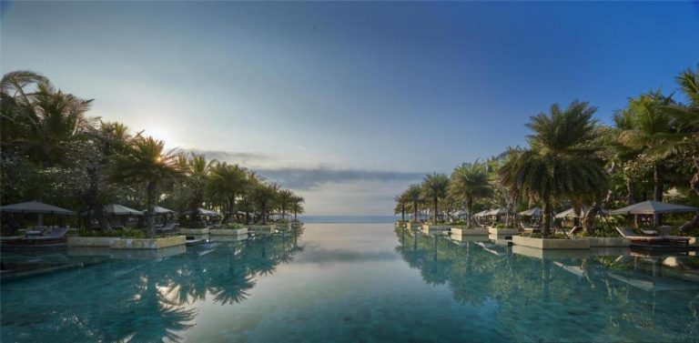 Piscina infinita con vistas al mar rodeada de palmeras tropicales en The Apurva Kempinski Bali