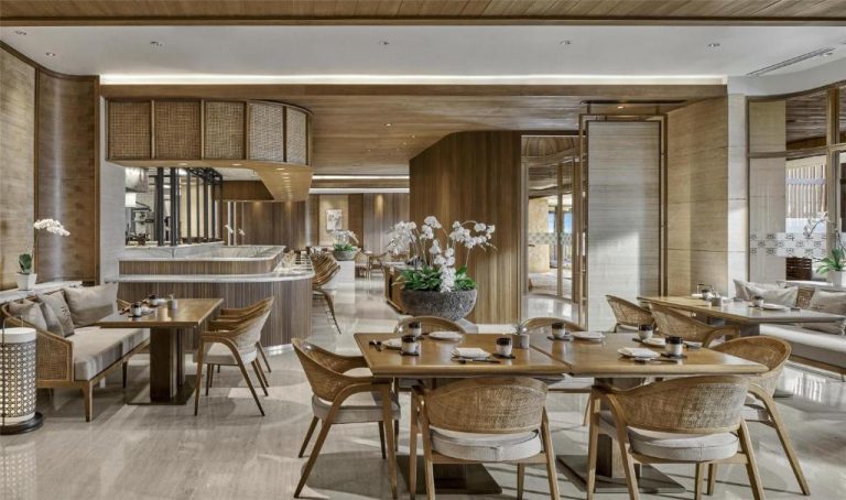 Elegante restaurante interior con mesas de madera y orquídeas blancas en The Apurva Kempinski Bali