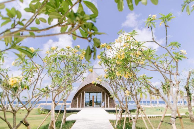 Capilla con arco de madera y jardín de frangipanis en The Apurva Kempinski Bali con vistas al océano