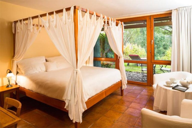 Habitación con cama dosel y cortinas blancas con vistas al jardín en el Hotel Atrio