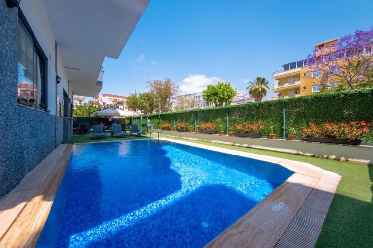 Piscina exterior con jardín y tumbonas del Pasham Residence rodeada de vegetación y flores