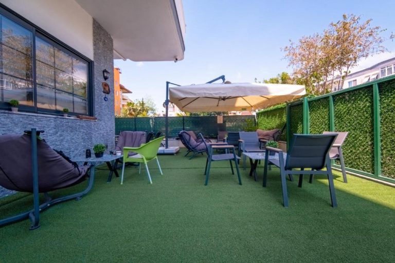 Terraza exterior con césped artificial, sillas y sombrilla en Pasham Residence
