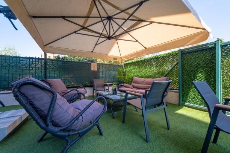 Terraza exterior con sillones, sombrilla y césped artificial en Pasham Residence