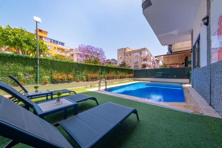 Piscina exterior con tumbonas y césped del Pasham Residence rodeada de jardín y edificios