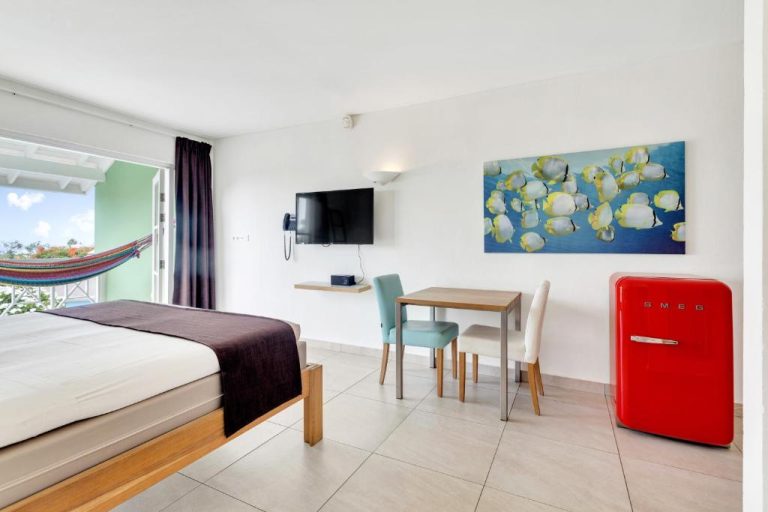 Habitación con cama doble, mininevera SMEG roja y balcón con hamaca en Chogogo Dive Beach Resort Curaçao