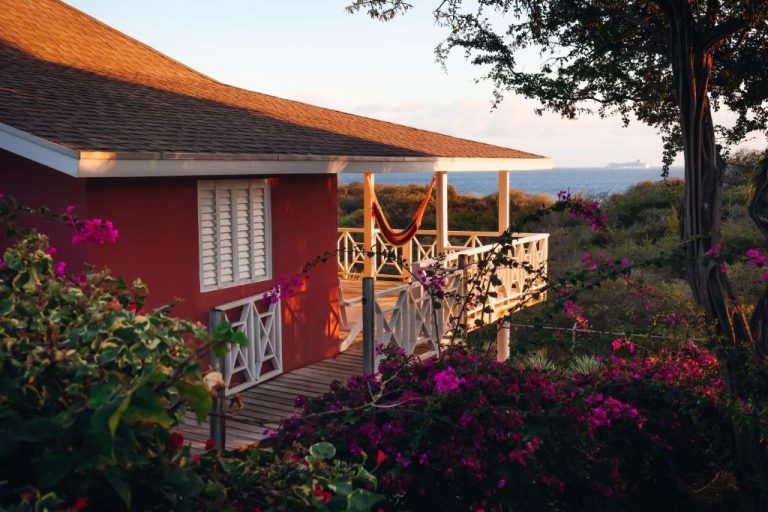 Bungalow rojo con terraza y hamaca rodeado de buganvillas y vistas al mar en Chogogo Dive & Beach Resort Curaçao