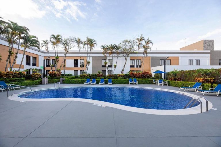 Piscina exterior con tumbonas azules del Holiday Inn Express San José Airport Costa Rica rodeada de palmeras