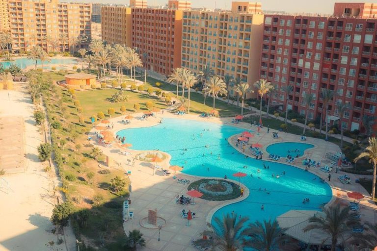 Vista aérea de la piscina exterior con forma libre del resort Porto Golf Marina rodeada de palmeras