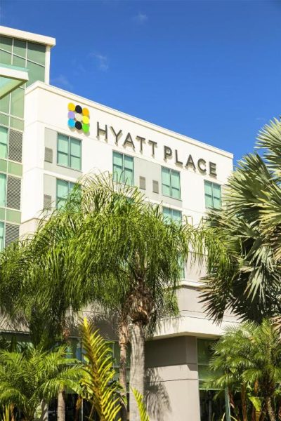 Fachada exterior del Hyatt Place Manatí rodeada de palmeras tropicales bajo un cielo azul despejado