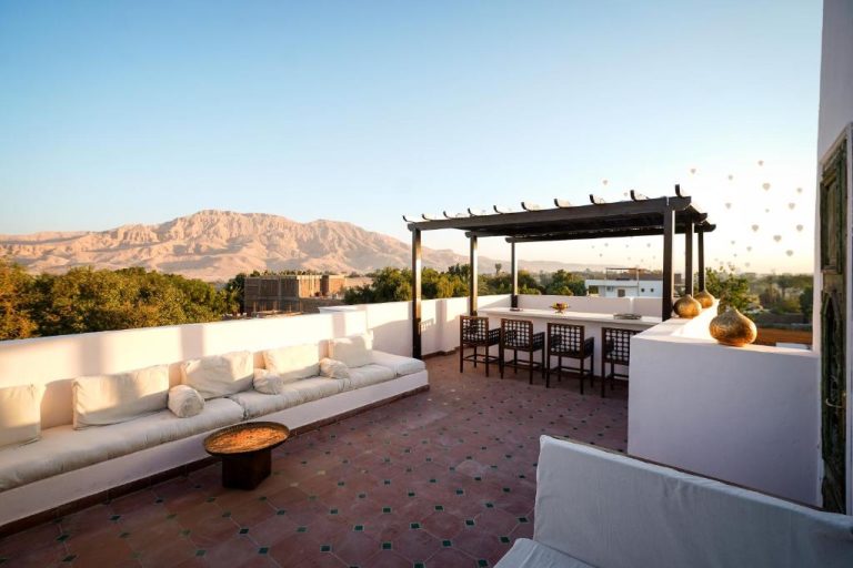 Terraza exterior con sofás blancos y pérgola del Al Wadi Hotel con vistas al desierto y montañas