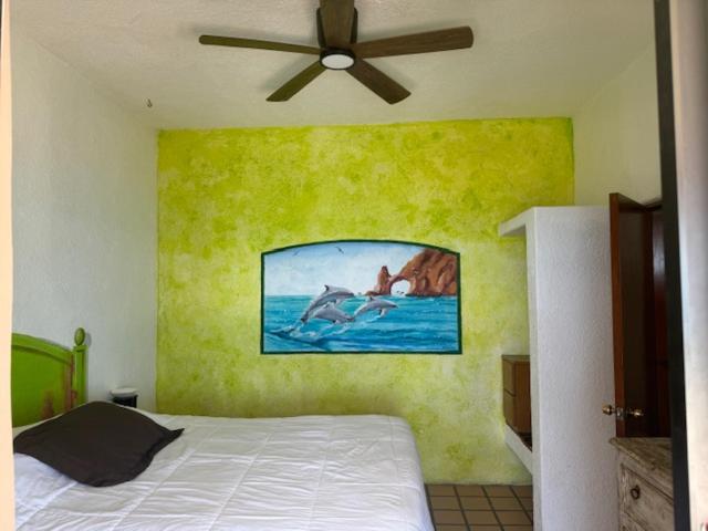 Habitación del Hotel Sauza con mural de delfines en pared verde y ventilador de techo