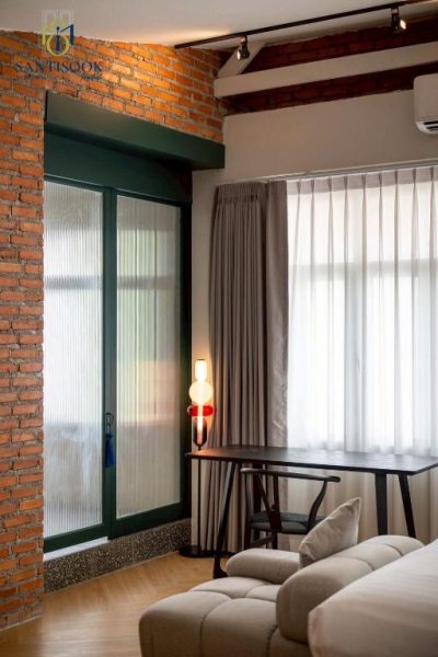 Habitación con escritorio, pared de ladrillo y ventanas con cortinas en Santisookmidtown Pattani