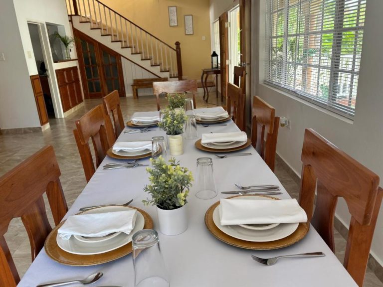 Comedor elegante con mesa larga preparada para cenar en Sommerville Resorts, decorada con vajilla blanca y plantas