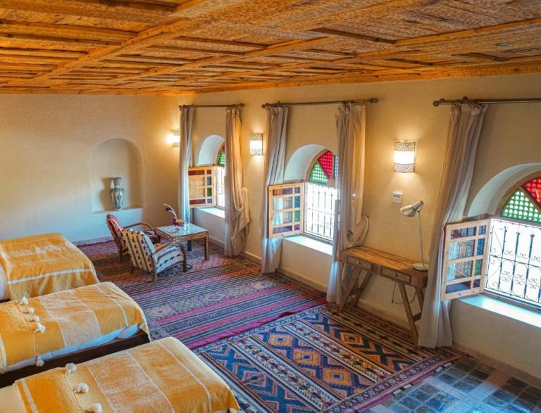 Habitación triple con decoración bereber, ventanas de colores y alfombras tradicionales en Kasbah Hnini