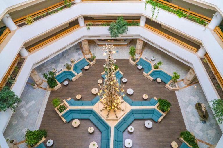 Amplio atrio interior del Hotel Sol Azur con sofás azules, chandelier central y vegetación tropical vista desde altura