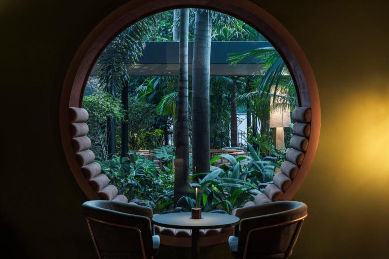 Salón íntimo con ventana circular y vista al jardín tropical en Hotel Poblado Plaza