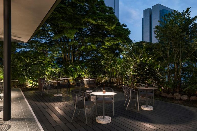 Terraza exterior con mesas y jardín tropical iluminado del Hotel Poblado Plaza al atardecer
