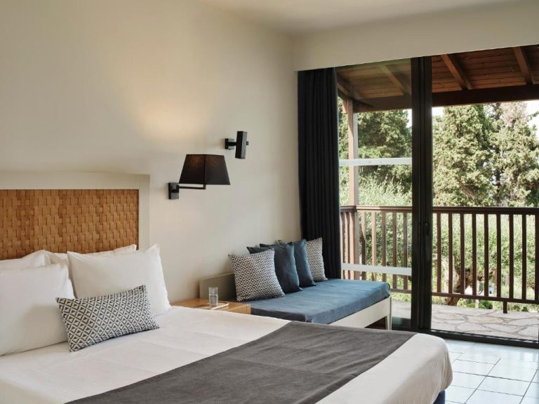 Habitación doble con cabecero de madera y balcón con vistas al jardín en Aeolos Beach Resort