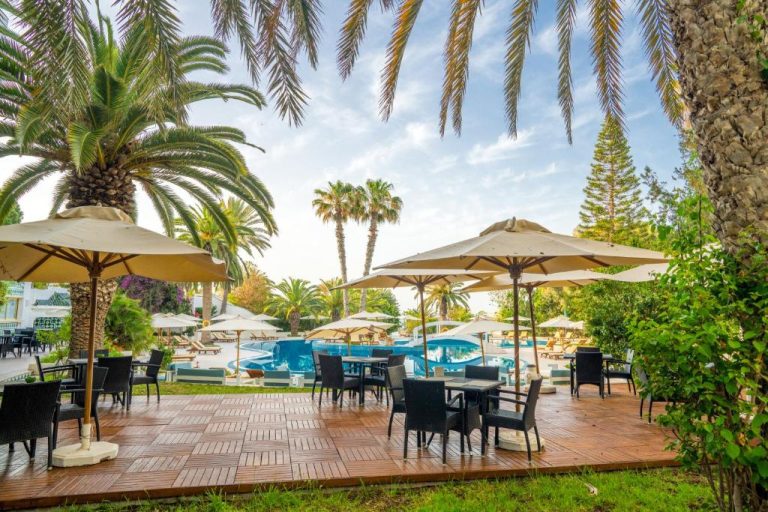 Terraza con mesas y sombrillas junto a la piscina exterior del Hotel Sol Azur rodeada de palmeras