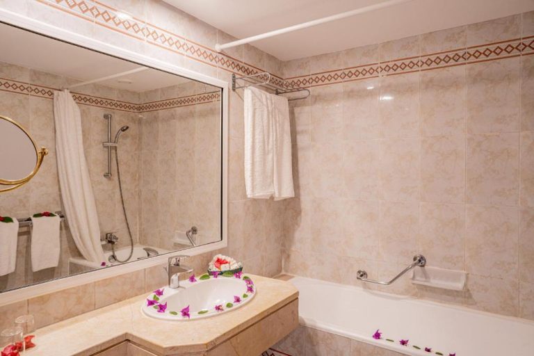 Baño completo con bañera, ducha y lavabo decorado con flores en el Hotel Sol Azur