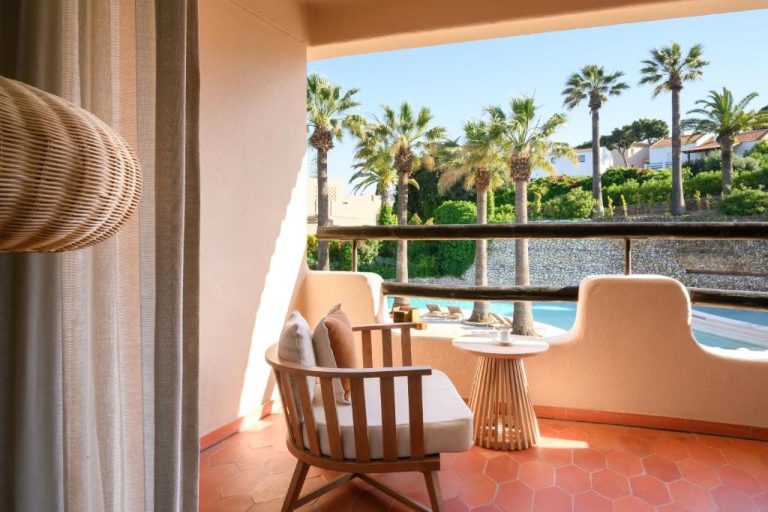Terraza privada con sillones y vistas a la piscina rodeada de palmeras en Vilalara Grand Hotel Algarve
