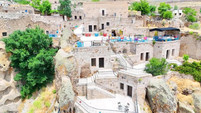 Terraza exterior con mesas coloridas del Hotel Kapadokya Ihlara Konakları entre formaciones rocosas de Capadocia