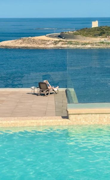 Piscina infinita con vistas al mar y terraza solarium del Qawra Palace Resort & SPA en Malta