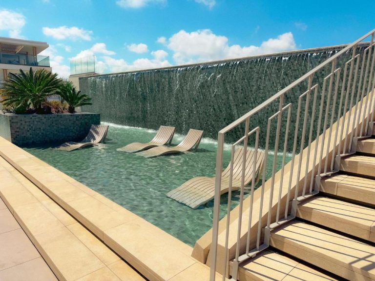Piscina con cascada de agua y tumbonas sumergidas en el Qawra Palace Resort & Spa de Malta