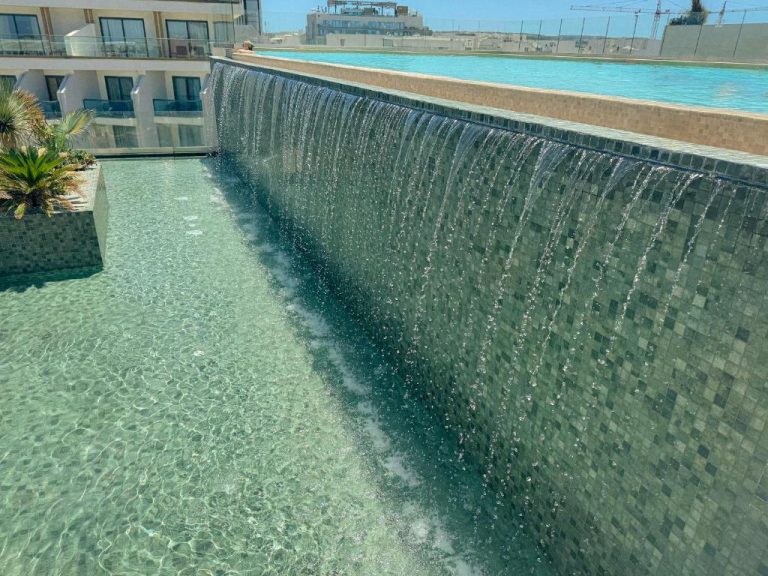 Cascada decorativa sobre mosaico en la piscina exterior del Qawra Palace Resort & SPA en Malta