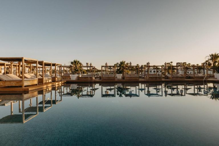 Piscina exterior con tumbonas y cabañas de madera al atardecer en Lago Resort Menorca Adults Only