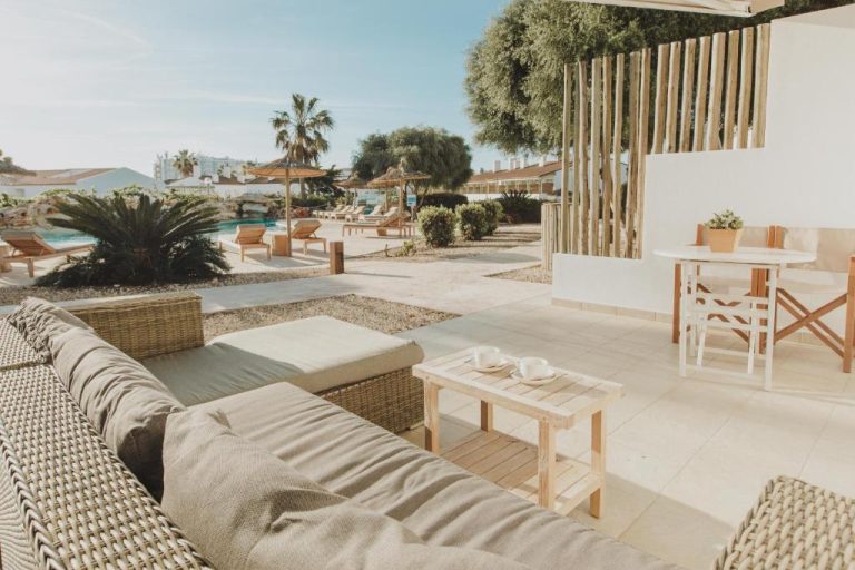 Terraza privada con sofás de ratán y vistas a la piscina exterior en Lago Resort Menorca Villas