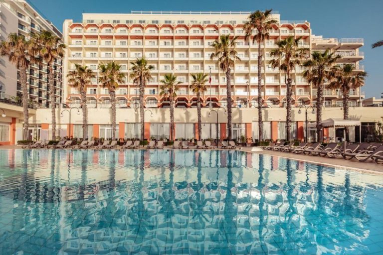 Piscina exterior con palmeras y tumbonas del Qawra Palace Resort & Spa en Malta