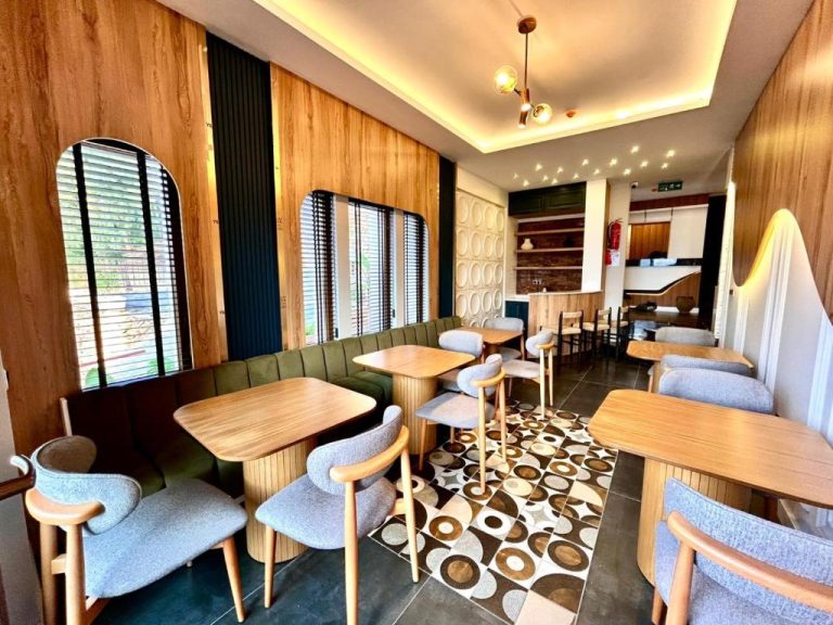 Salón restaurante moderno con mesas de madera y sofás verdes en Castello by Mediterra Hotel