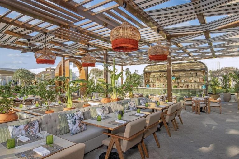 Terraza restaurante del Conrad Dubai con pérgola de madera, plantas tropicales y lámparas de mimbre