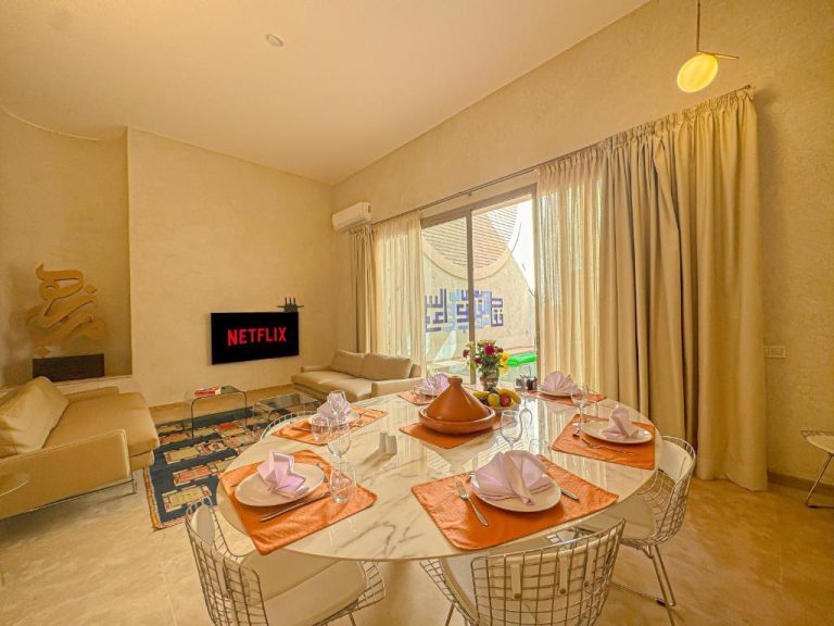 Salón comedor elegante con mesa de mármol y TV Netflix en Riad Timija Marrakech