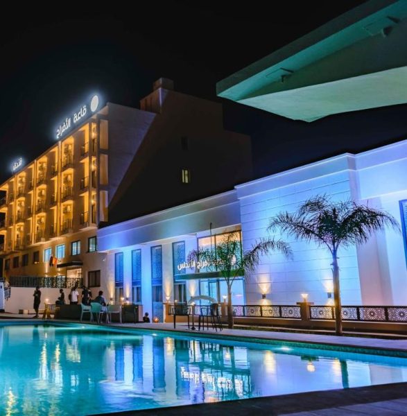 Piscina exterior iluminada del Hotel Rherssllah con vistas a la fachada y salón de eventos de noche